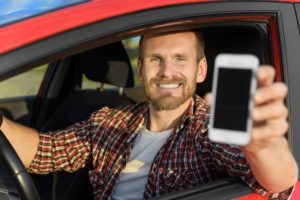 Man in car driving showing smart phone.